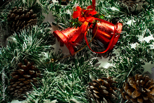 Red Christmas bells on green tinsel, and cones around. photo