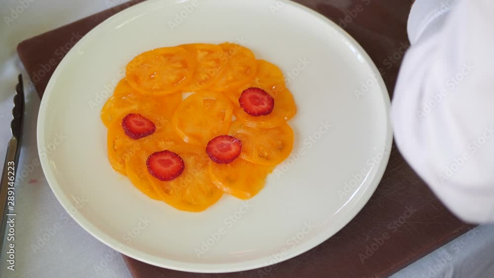 A cook in black gloves lays strawberries on yellow tomatoes. A cook in black gloves lays strawberries on yellow tomatoes.
