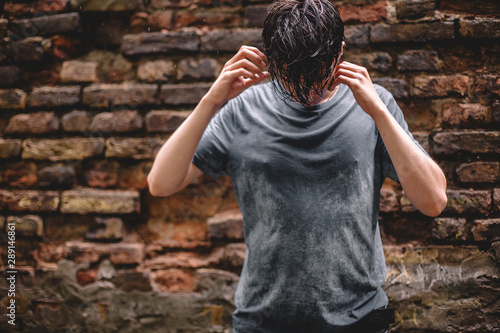 Fényképezés Worried anxious young man with his head down standing in the rain against brick