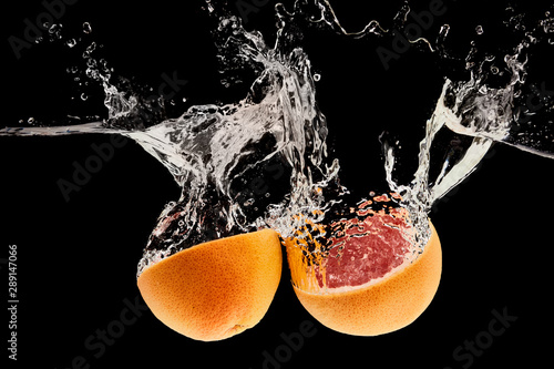 Fototapeta Naklejka Na Ścianę i Meble -  ripe natural grapefruit halves falling in water with splash isolated on black