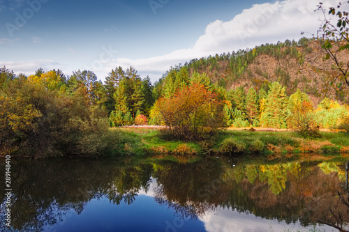 Autumn river with reflecting trees against the backdrop of forests and mountains.