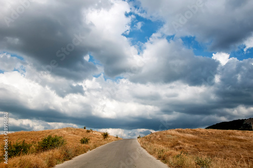 Rural dirt road along the picturesque yellow fields before the rain.Big beautiful white clouds