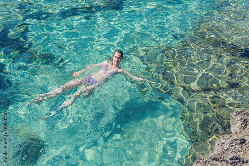 Aerial view of young woman in bright bikini is swimming in the transparent  blue sea. Top view of slim woman floating on water of Mediterranean  sea.