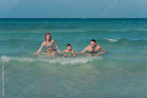 Family of three people getting out from sea water together. They smiling and enjoying thier summere vacations. Front view.