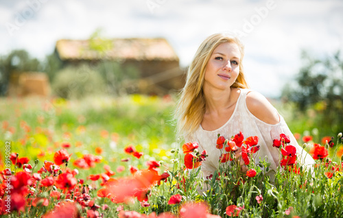 Beautiful young female in white dress in poppy field of wild flowers
