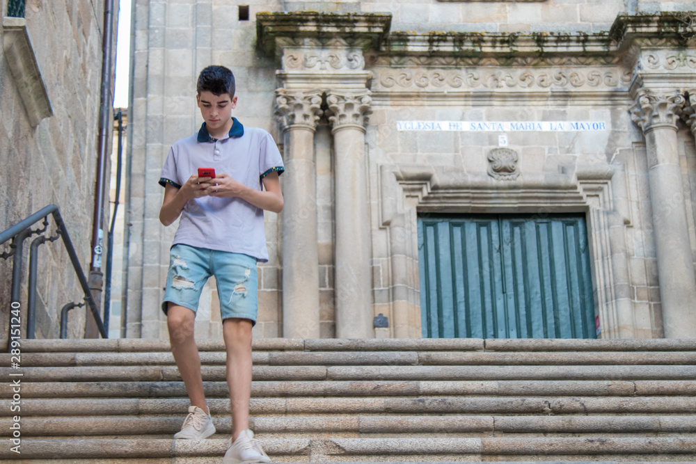 young teenage man with mobile phone walking in the city