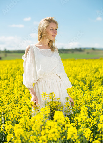 Young woman in yellow oilseed rape field posing in white dress