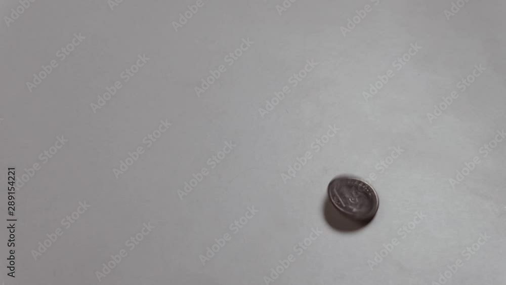 The American dime coin spins around its axis and moves from top to bottom. Heads or tails. A male hand raises a coin with the inscription Liberty on a white table. The American dime coin spins around its axis and moves from top to bottom. Heads or tails. A male hand raises a coin with the inscription Liberty on a white table.