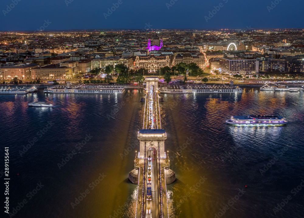 Budapest, Hungary - Aerial view of illuminated Szechenyi Chain Bridge with St. Stephen's Basilica, ferris wheel and cruise ships on River Danube at blue hour on a nice summer evening