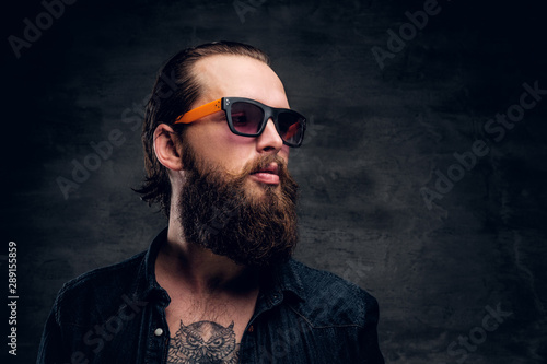 Handsome bearded man in sunglasses is posing for photographer at dark photo studio.