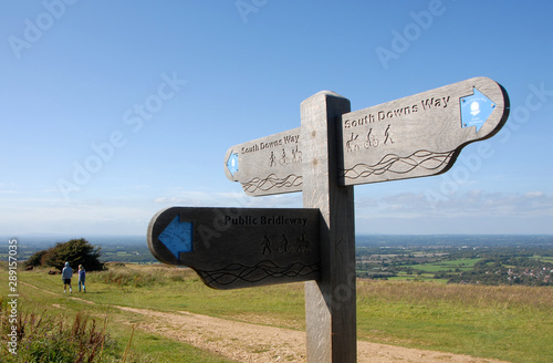 South Downs National Park, Sussex, England, UK. A man and a woman walking on the South Downs way in Sussex. A signpost shows the route of the South Downs Way and views over the Sussex Weald.