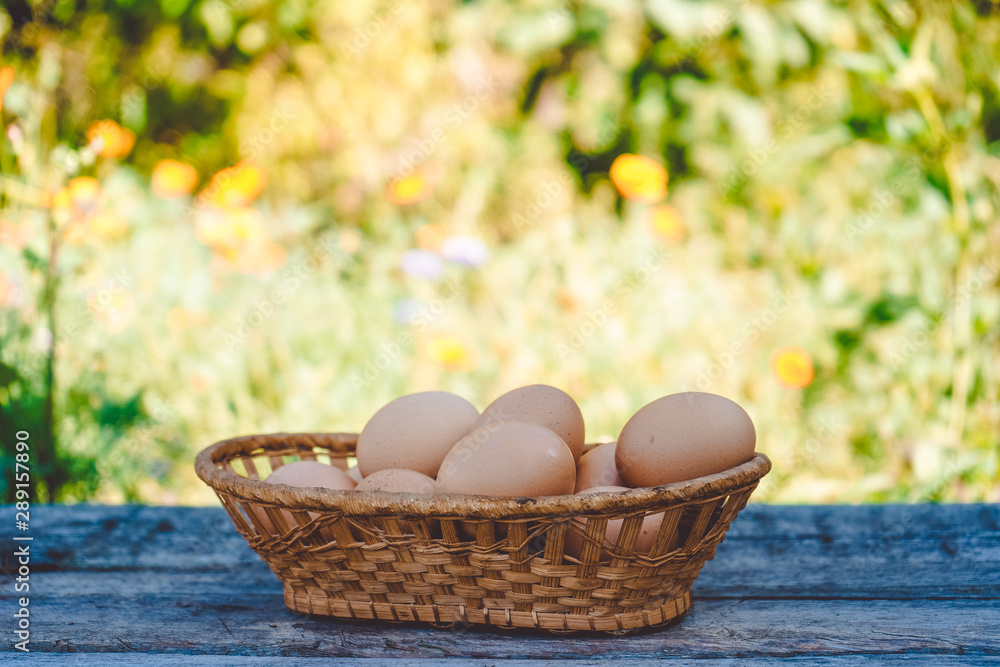 Beautiful chicken eggs in a wicker basket on a wooden Board against a landscape of greenery and flowers. Beautiful chicken eggs in a wicker basket on a wooden Board against a landscape of greenery and flowers.