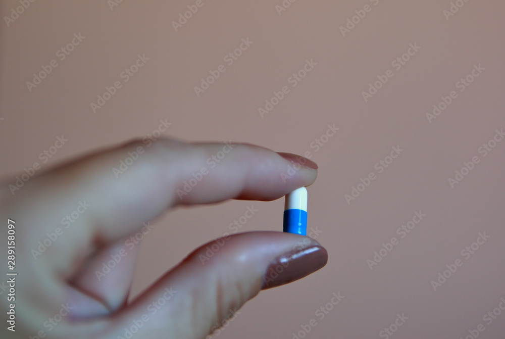 femal hand close up holdins double color tablet / pill / capsule isolated on light pink background femal hand close up holdins double color tablet / pill / capsule isolated on light pink background