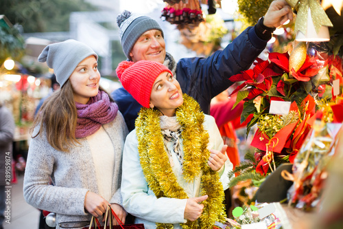 mature mother, father and teen girl buying red Euphorbia and floral decorations at Christmas fair