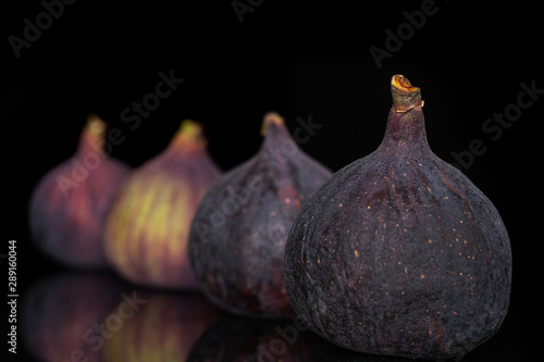 Group of four whole fresh fig fruit in row isolated on black glass photo