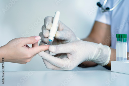 Doctor checking blood sugar level, doctor using lancelet on finger, testing blood glucose