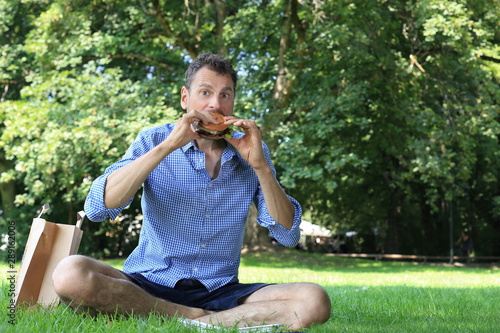 Mann beisst genuesslich in Hamburger im Park photo