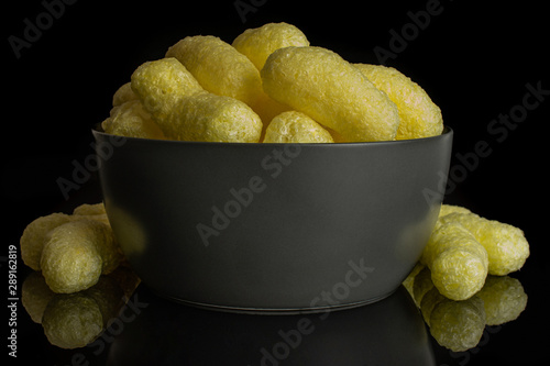 Lot of whole salted yellow corn puff in gray ceramic bowl isolated on black glass