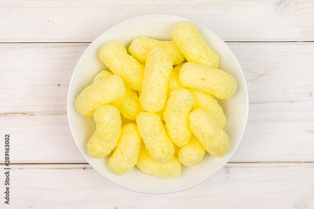 Lot of whole salted yellow corn puff on white ceramic plate flatlay on white wood Lot of whole salted yellow corn puff on white ceramic plate flatlay on white wood