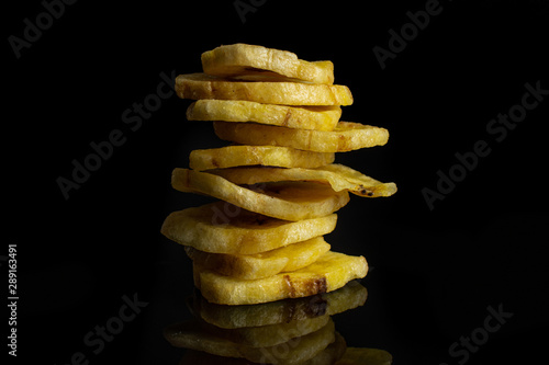 Lot of slices of sweet yellow dry banana in column isolated on black glass