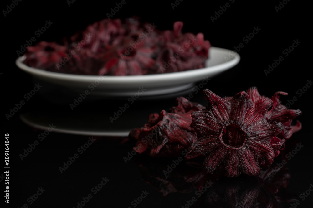 Lot of whole sweet red candied hibiscus small group is aside and the rest is on white ceramic plate isolated on black glass Lot of whole sweet red candied hibiscus small group is aside and the rest is on white ceramic plate isolated on black glass