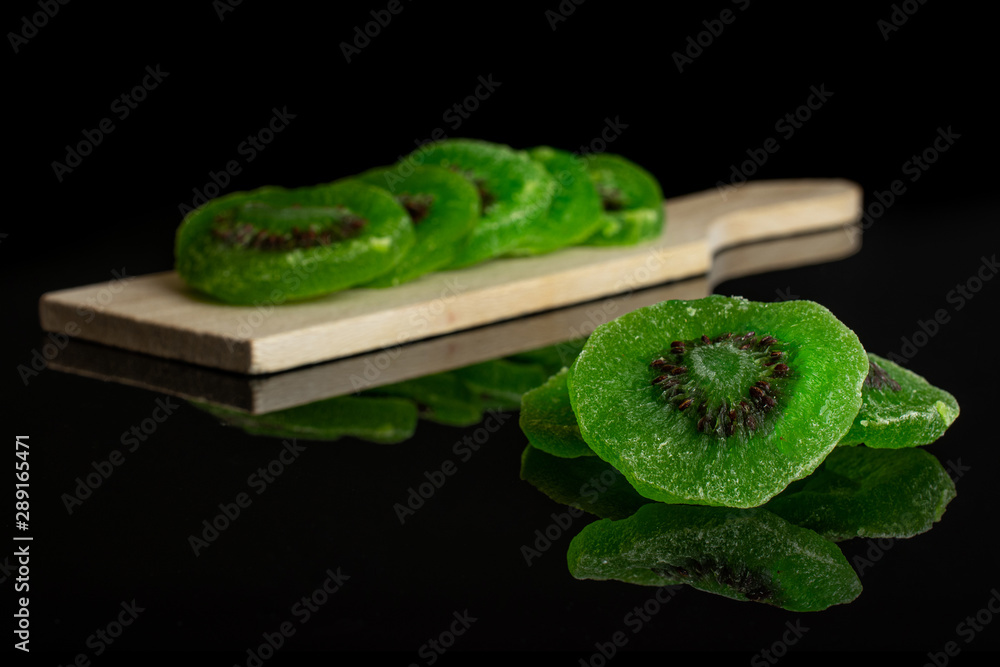 Group of eight slices of sweet green candied kiwifruit on small wooden cutting board isolated on black glass Group of eight slices of sweet green candied kiwifruit on small wooden cutting board isolated on black glass