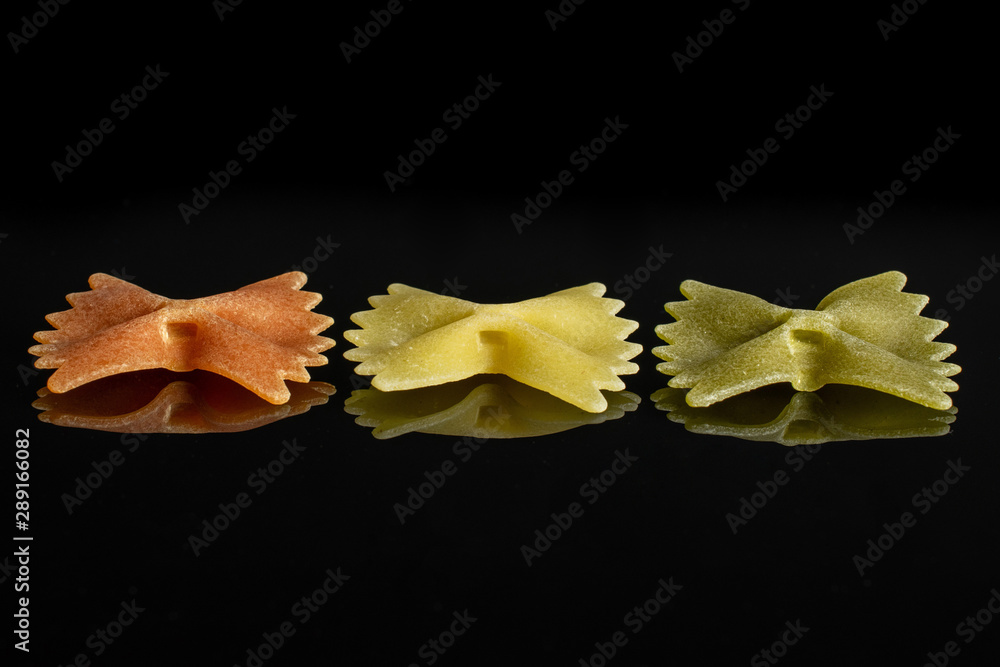 Group of three whole red, yellow and green uncooked farfalle isolated on black glass Group of three whole red, yellow and green uncooked farfalle isolated on black glass