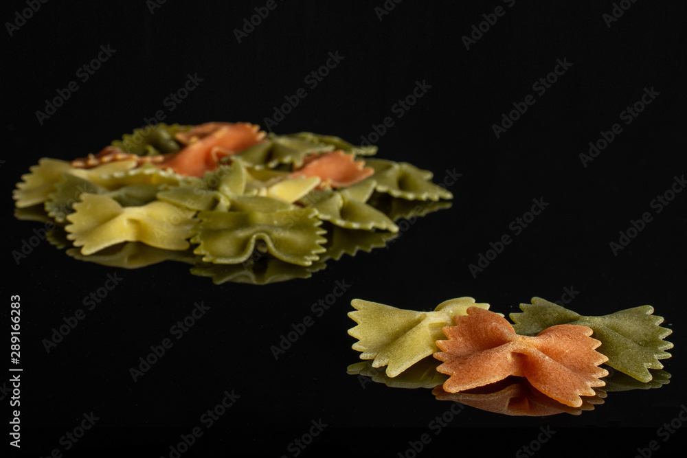 Lot of whole red, yellow and green uncooked farfalle three are in the front isolated on black glass Lot of whole red, yellow and green uncooked farfalle three are in the front isolated on black glass