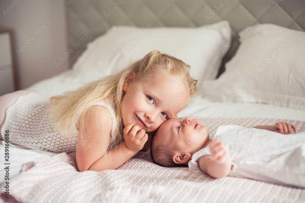 Young beautiful mother holds a baby. Little sister kisses her little sister. Baby. Children bedroom. Young beautiful mother holds a baby. Little sister kisses her little sister. Baby. Children bedroom.