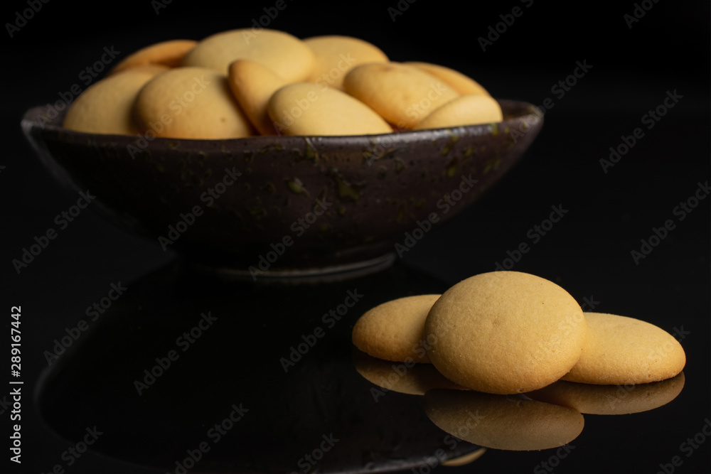 Lot of whole sweet golden sponge biscuit in dark ceramic bowl isolated on black glass