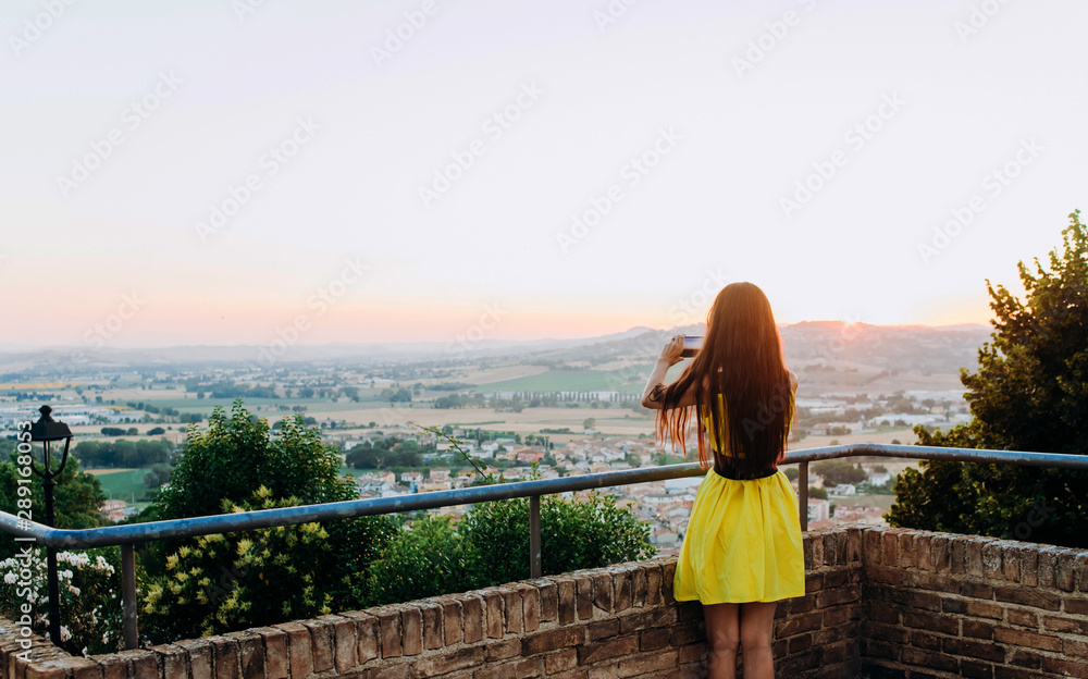 Fototapeta premium Girl in yellow dress takes pictures of landscapes