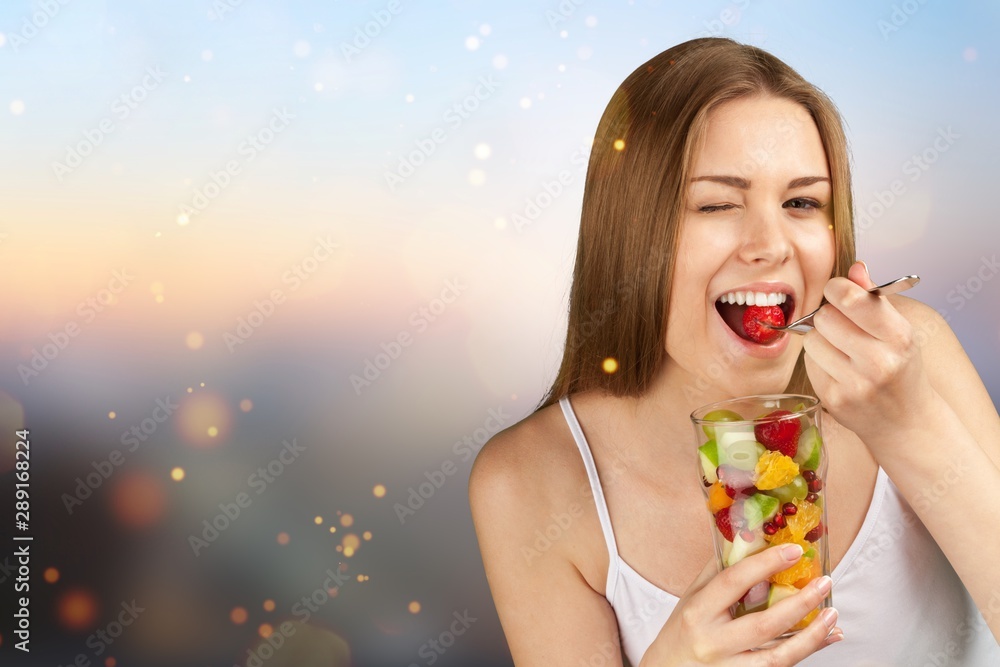 Young woman eating fruits from glass on blurred background Young woman eating fruits from glass on blurred background