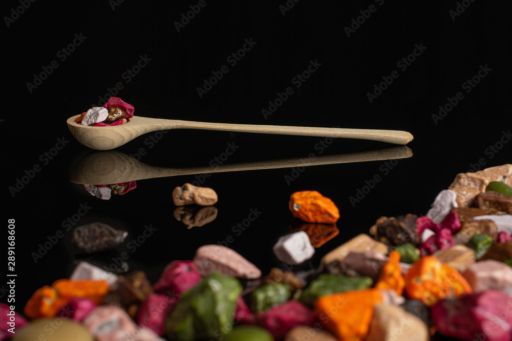 Lot of whole sweet chocolate stone in a wooden spoon isolated on black glass Lot of whole sweet chocolate stone in a wooden spoon isolated on black glass