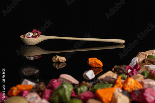 Lot of whole sweet chocolate stone in a wooden spoon isolated on black glass