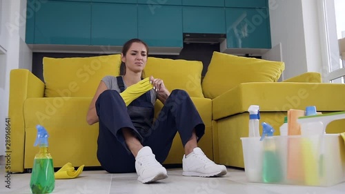 Tired female cleaner sitting near the couch and feeling enfeebled after washing wooden floor photo