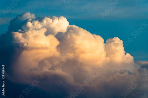 Cloudscape of dramatic white fluffy cumulus clouds illuminated by evening light contrasted with blue sky