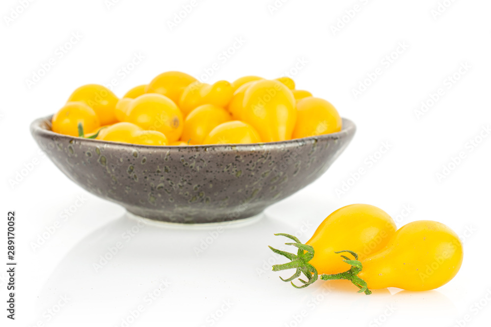 Lot of whole fresh yellow pear tomato in dark ceramic bowl isolated on white background Lot of whole fresh yellow pear tomato in dark ceramic bowl isolated on white background