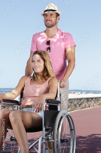 man pushing his wife in her wheelchair along seaside promenade