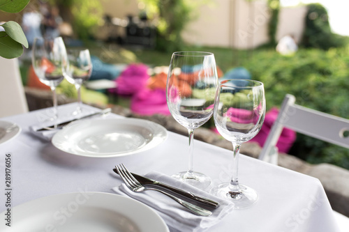 Wedding table setting decorated with fresh flowers in a brass vase. Wedding floristry. Banquet table for guests outdoors with a view of green nature. Bouquet with roses, eustoma and eucalyptus leaves