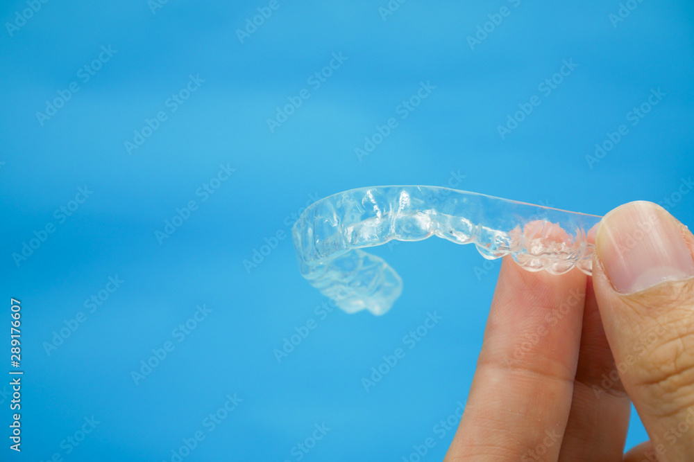 hand holding clear plastic retainer teeth that isolated on blue sky  background. it's an equipment for orthodontist give the patient to  orthodontic surgery in dental clinic or hospital Stock Photo | Adobe