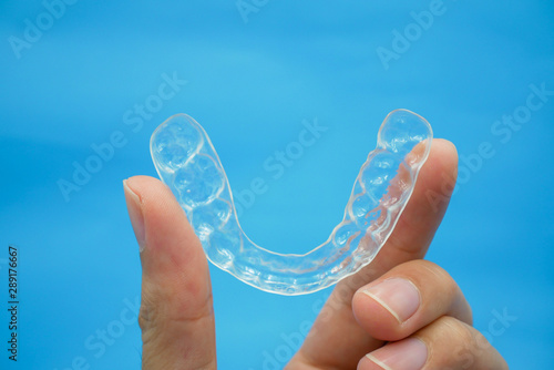 hand holding clear plastic retainer teeth that isolated on blue sky background. it's an equipment for orthodontist give the patient to orthodontic surgery in dental clinic or hospital
