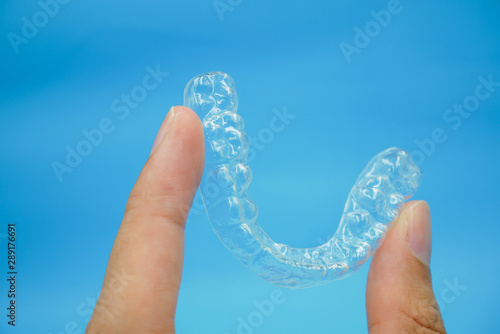 hand holding clear plastic retainer teeth that isolated on blue sky background. it's an equipment for orthodontist give the patient to orthodontic surgery in dental clinic or hospital