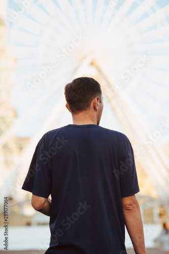 Ukrainian man in a navy-blue t-shirt standing in front of bright ferris wheel at Poshtova Plosca in Kyiv, Ukraine 