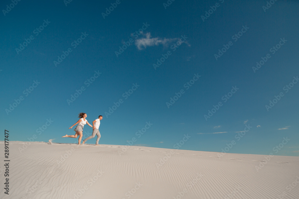 Fototapeta premium Romantic couple in love running on white sand in desert.