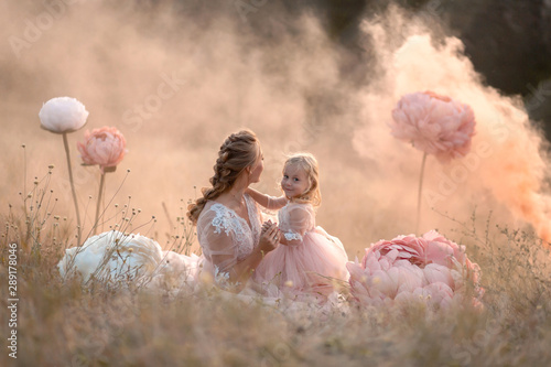 A little girl hugs mom sitting in a field surrounded by unreal big pink decorative flowers