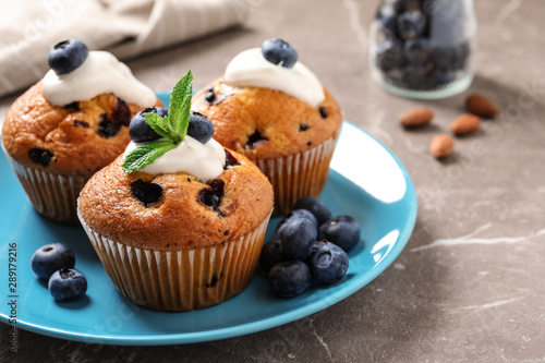 Plate of tasty muffins and blueberries on marble table