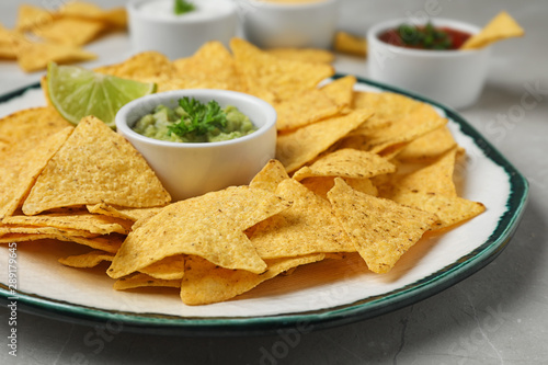 Plate of Mexican nacho chips with sauce on grey marble table, closeup