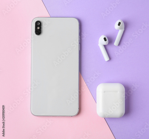 Wireless earphones, mobile phone and charging case on color background, flat lay