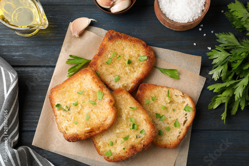 Slices of delicious toasted bread with garlic and herbs on blue wooden table, flat lay