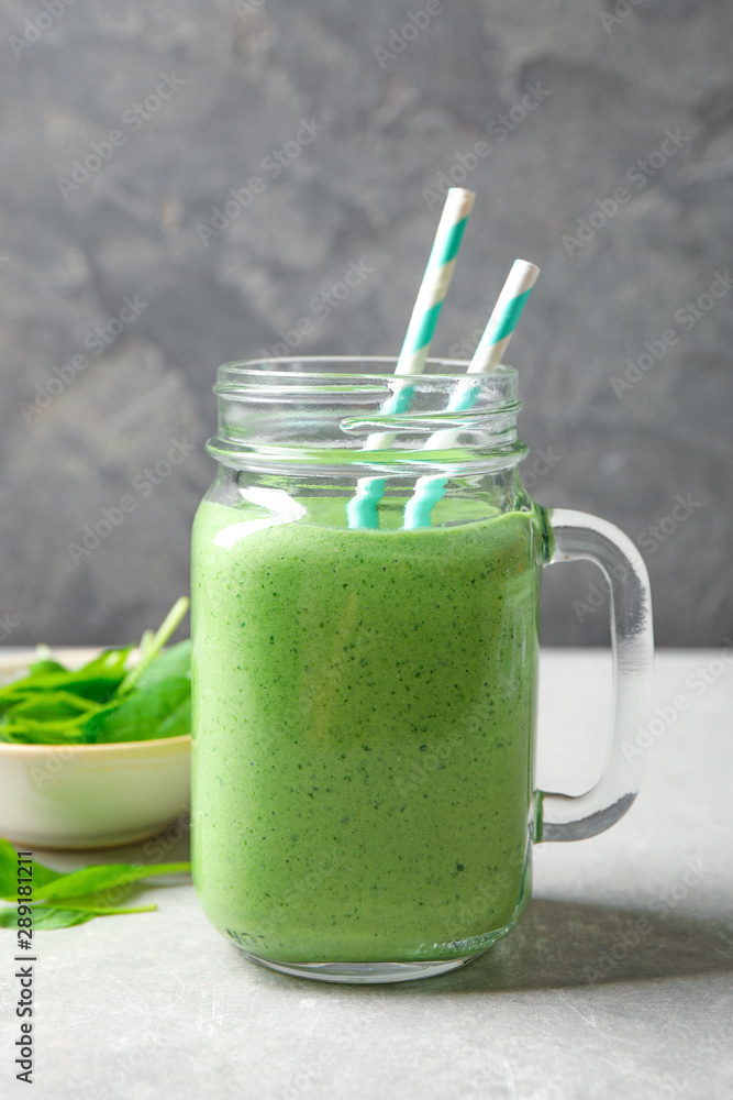 Mason jar of healthy green smoothie with fresh spinach on grey table Mason jar of healthy green smoothie with fresh spinach on grey table